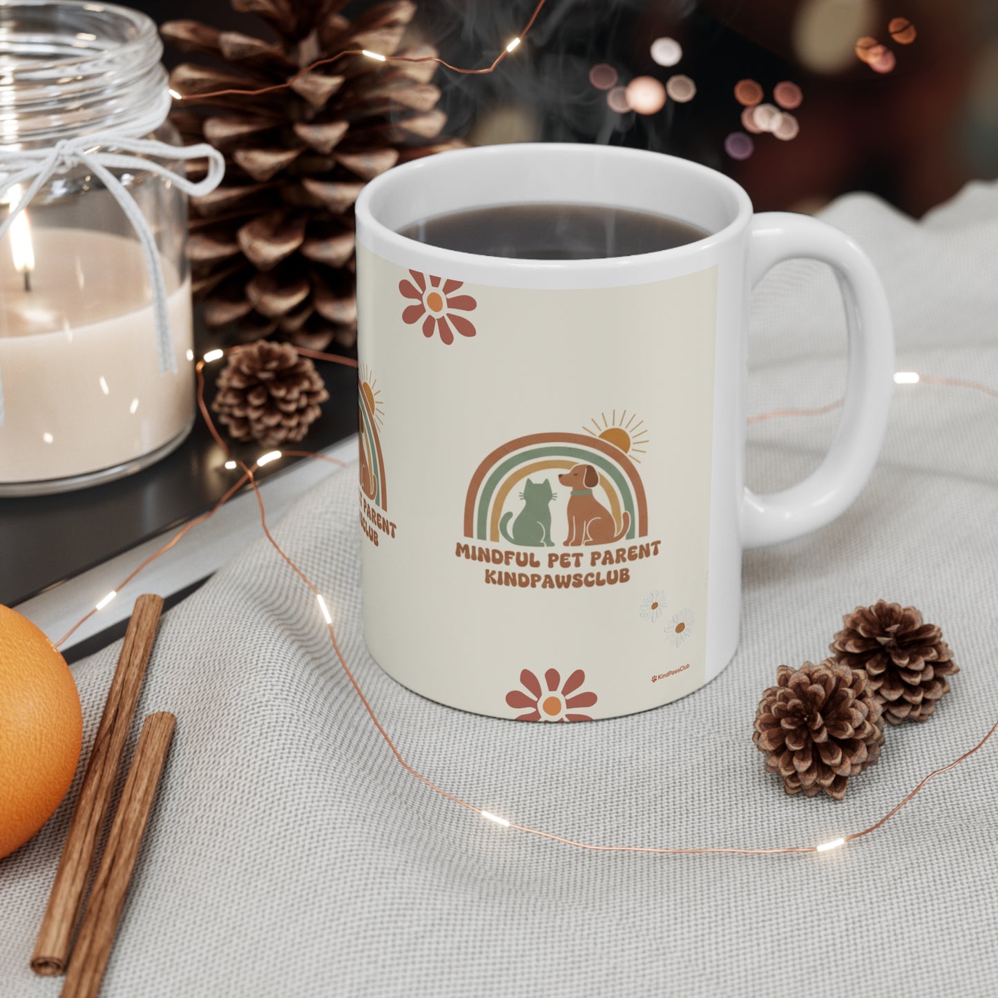 White mug with a design featuring two dogs and text, placed on a surface with decorative items like pine cones and an orange.