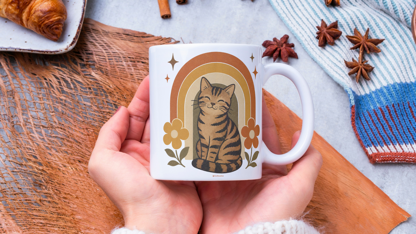 Person holding a mug with a cat illustration on a wooden surface with cinnamon sticks and a croissant.